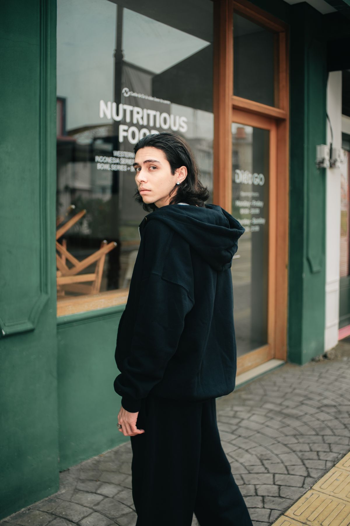 Model in a plain black hoodie outside a shopfront