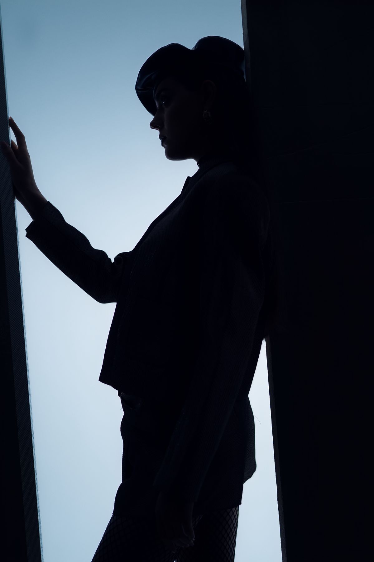 Silhouette of a model in a hoodie against a blue wall